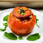 Greek Stuffed tomato on a white plate with mint leaves.