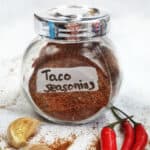 A jar of whole30 taco seasoning next to garlic and red chilis.
