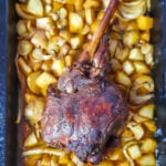 Greek leg of lamb roast on a bed of potatoes and fennel, in a black baking dish.