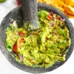 Guacamole in a molcajete surrounded by tortilla chips and ingredients.