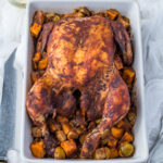 Slow roasted chicken in a white casserole dish with vegetables.
