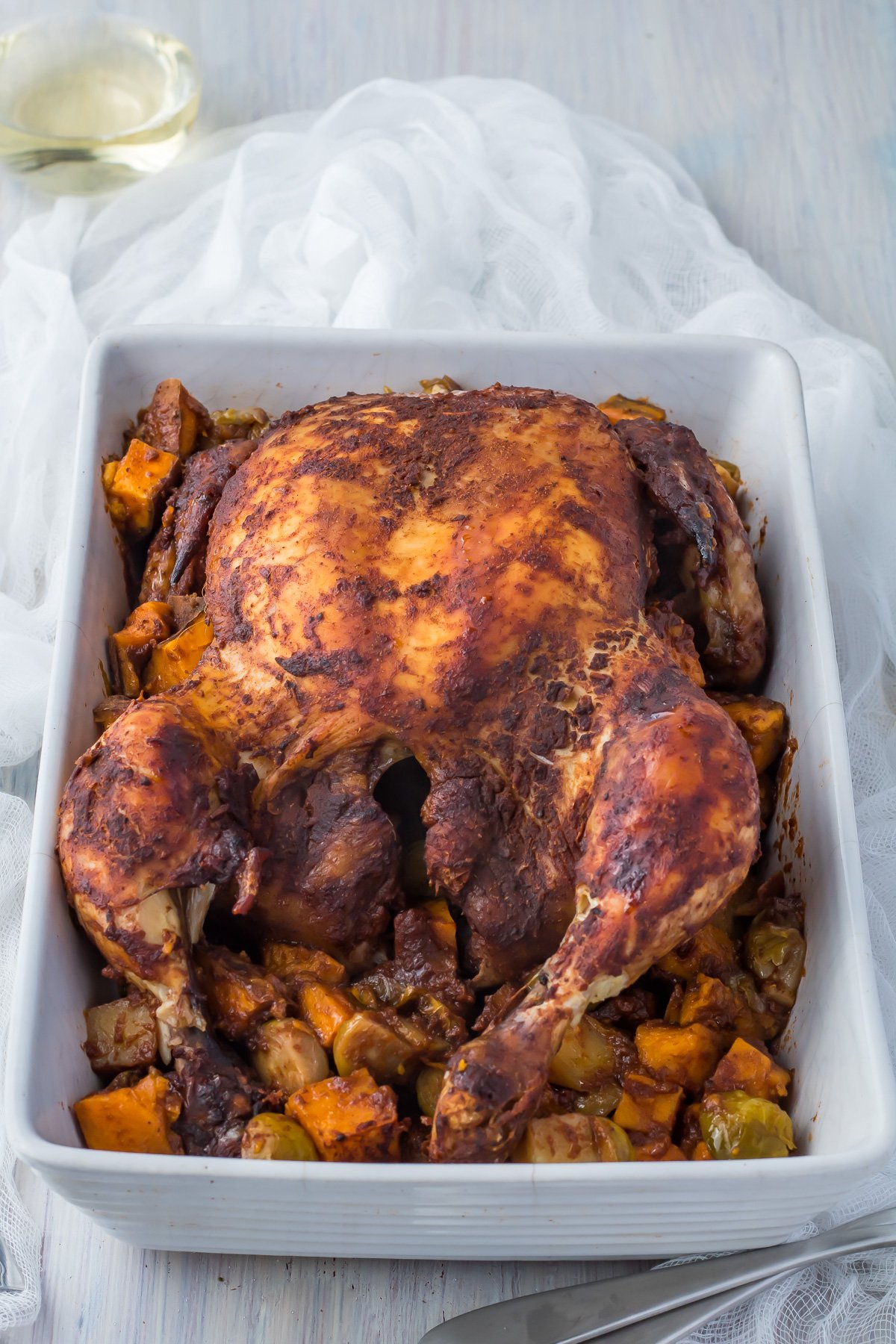 Slow roasted chicken in a white casserole dish with vegetables.