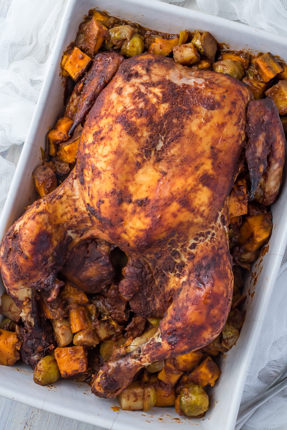 Overhead shot of roasted chicken in a white dish with vegetables.