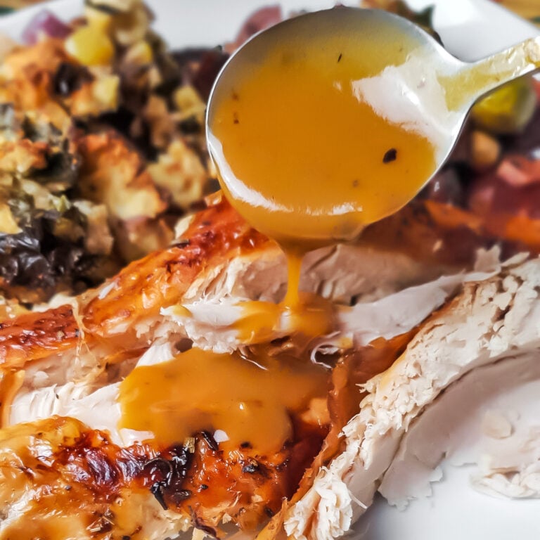 A spoon pouring gluten free turkey gravy over roasted turkey.