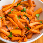 Air fryer carrots in a white bowl next to bowl of parsley and carrots.