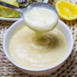 Avgolemono Sauce dripping from a spoon into a white bowl.