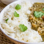 Bowl of instant pot basmati rice with curry, dry rice behind, on rattan placemat.