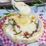 Spoon pulling melted cheese out of baked camembert.