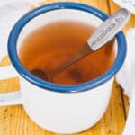 Cup of sumac tea in a white mug with a blue rim and a spoon inside.