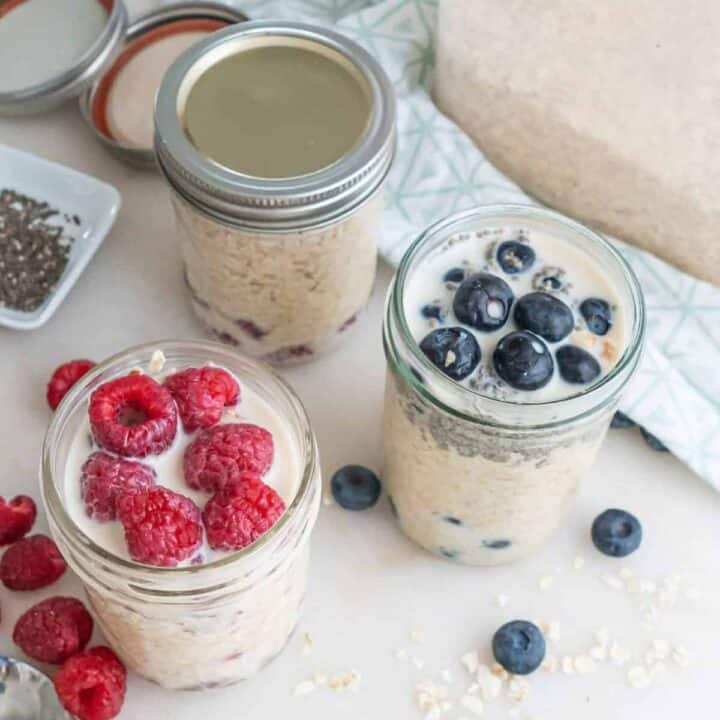 Small jars of overnight oats with raspberries and blueberries on a white tablecloth.