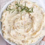 Overhead shot of mashed potatoes in a white bowl garnished with rosemary.