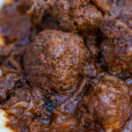 Close up of meatball in gravy over mashed potatoes.