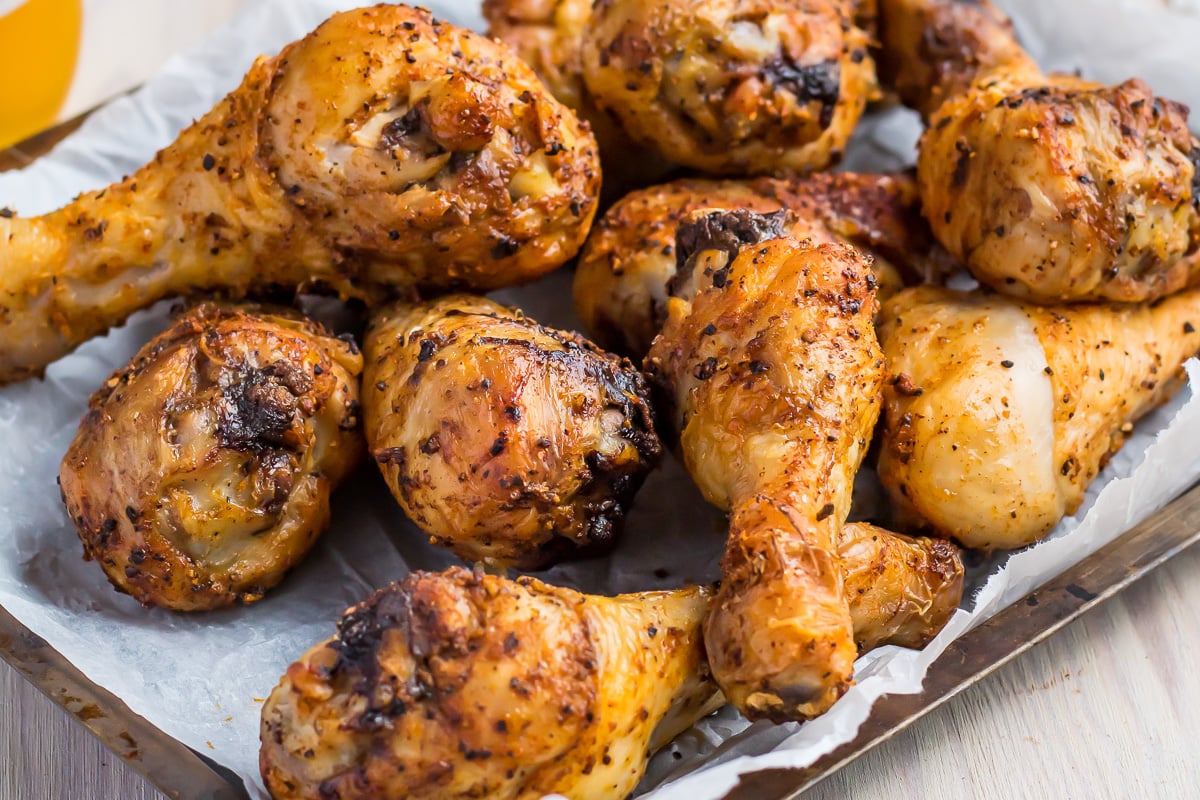 A tray filled with several air fryer chicken drumsticks, seasoned with spices and herbs, resting on parchment paper. The drumsticks appear golden-brown and crispy, suggesting they are freshly cooked.