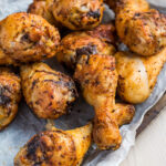 Close-up of crispy, air fryer chicken drumsticks with a golden-brown, seasoned crust, arranged on crinkled parchment paper. The chicken is visually appealing with a mix of crispy skin and tender meat, showcasing a homemade, flavorful dish.