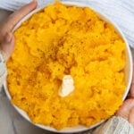 Overhead picture of hands holding a bowl of mashed rutabaga next to a white cloth.