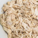 Overhead shot of shredded chicken in a white bowl.