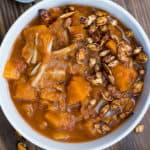 A slow cooker vegetable stew with pumpkin and nuts on top.