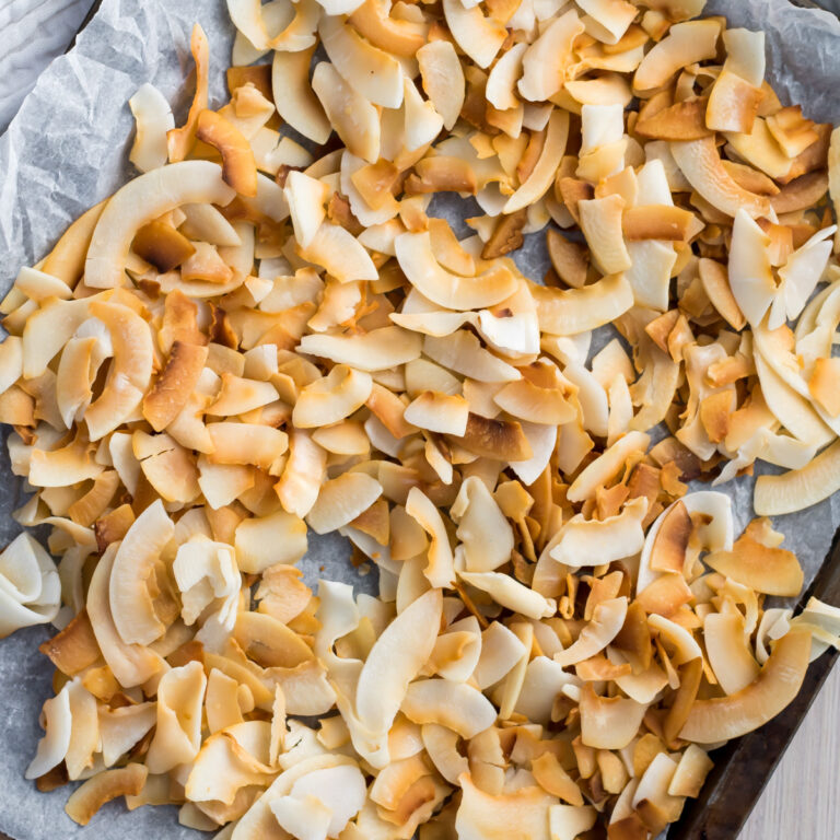 Toasted coconut chips are scattered on a parchment-lined baking sheet.
