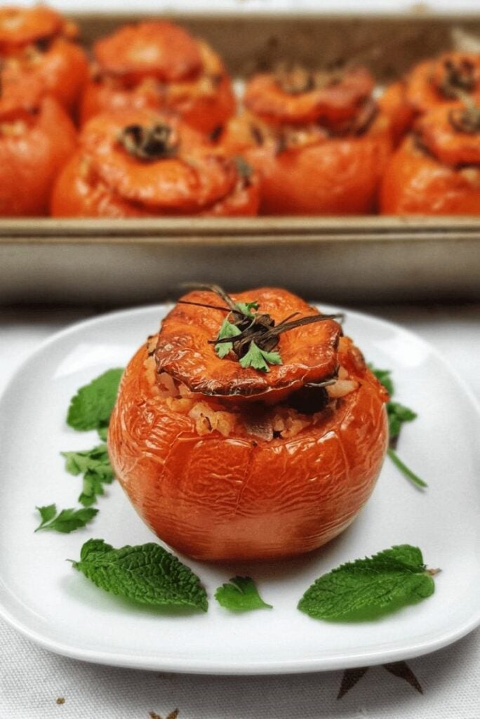 Stuffed tomatoes on a white plate with mint leaves.