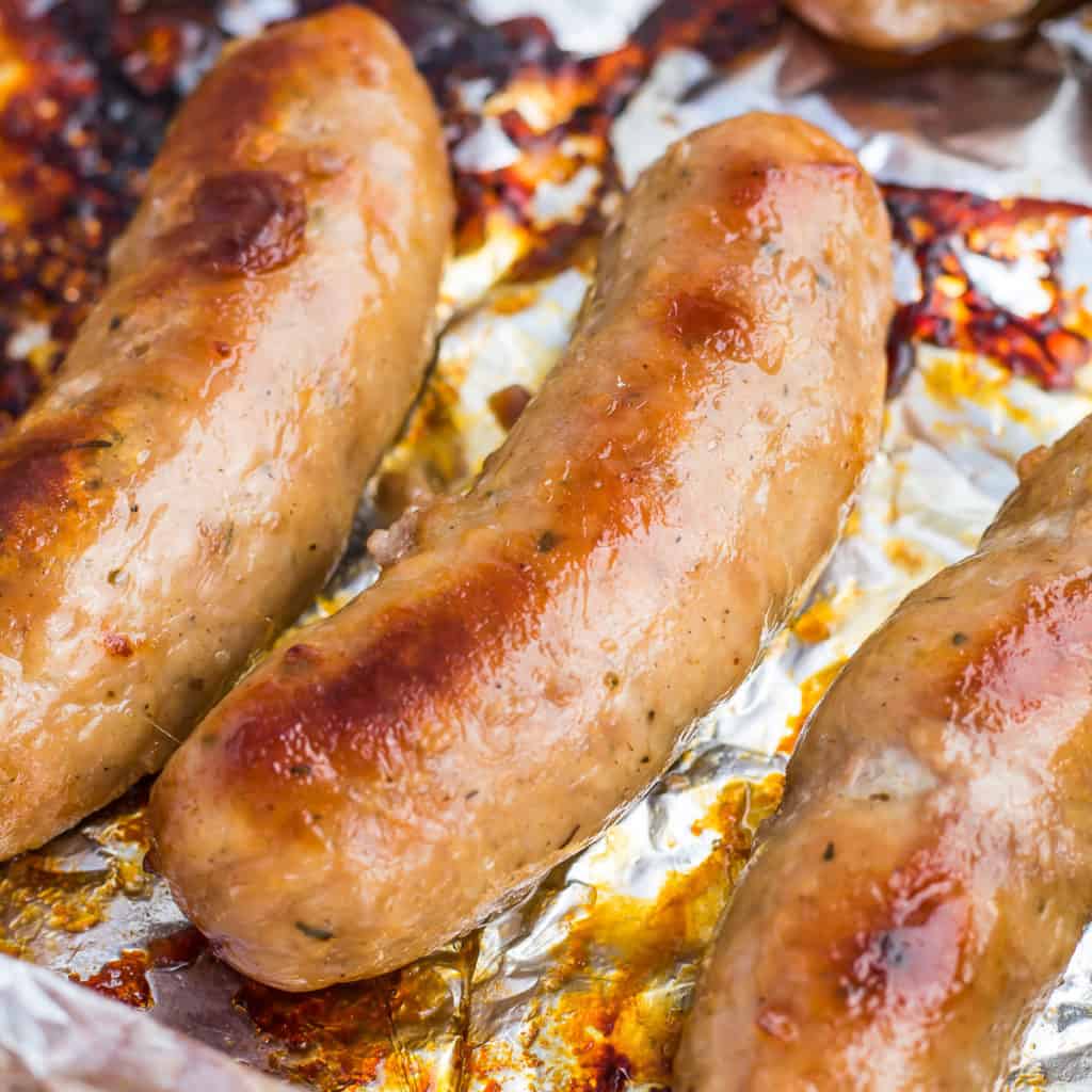 Sausage links on top of aluminium on a baking tray.