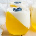 Yellow keto jello with whipped cream in a stemless wine glass garnished with blueberries.