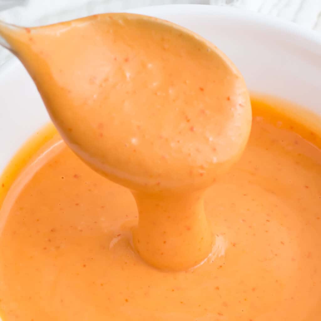 Spoon dripping spicy mayo into a white bowl.