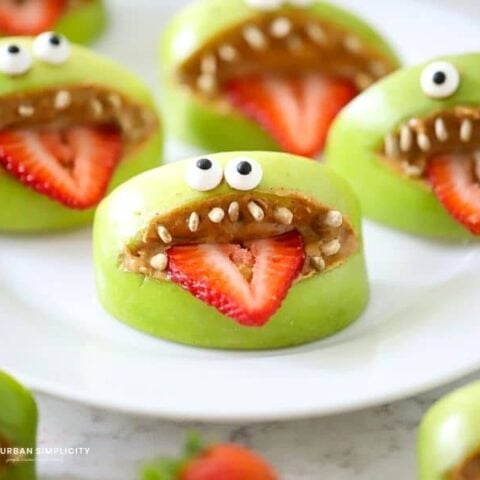 A plate with green apples and strawberries with monster faces on them.