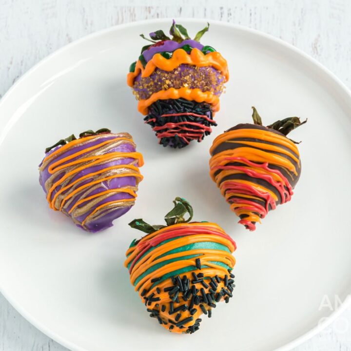 Four colorfully decorated strawberries on a white plate.