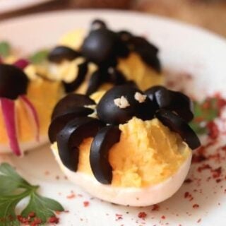 Deviled eggs with spiders on a plate.