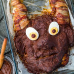 Monster meatloaf in a baking dish next to ketchup with a pastry brush.