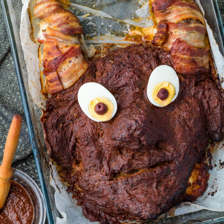 Monster meatloaf in a baking dish next to ketchup with a pastry brush.