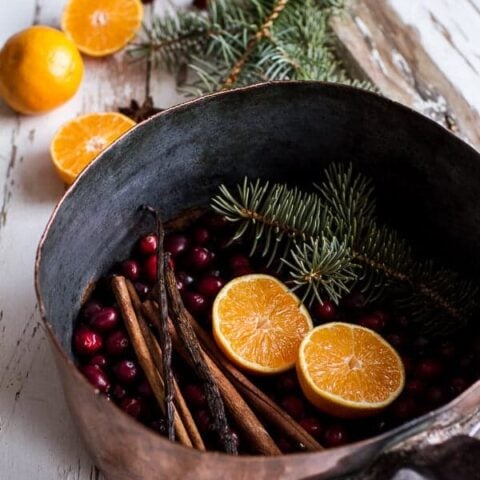 A Christmas simmer pot recipe featuring a copper pan filled with cinnamon sticks, oranges, and cranberries.