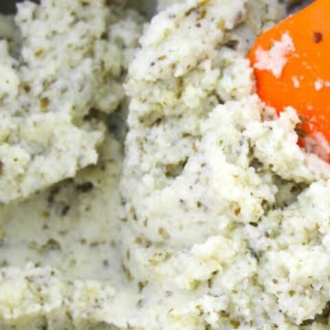 Keto mashed potatoes in a bowl with an orange spatula, perfect for Christmas side dishes.