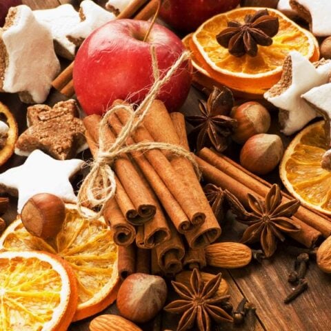 Christmas simmer pot recipes with cinnamon, apples, oranges and spices placed on a wooden table.