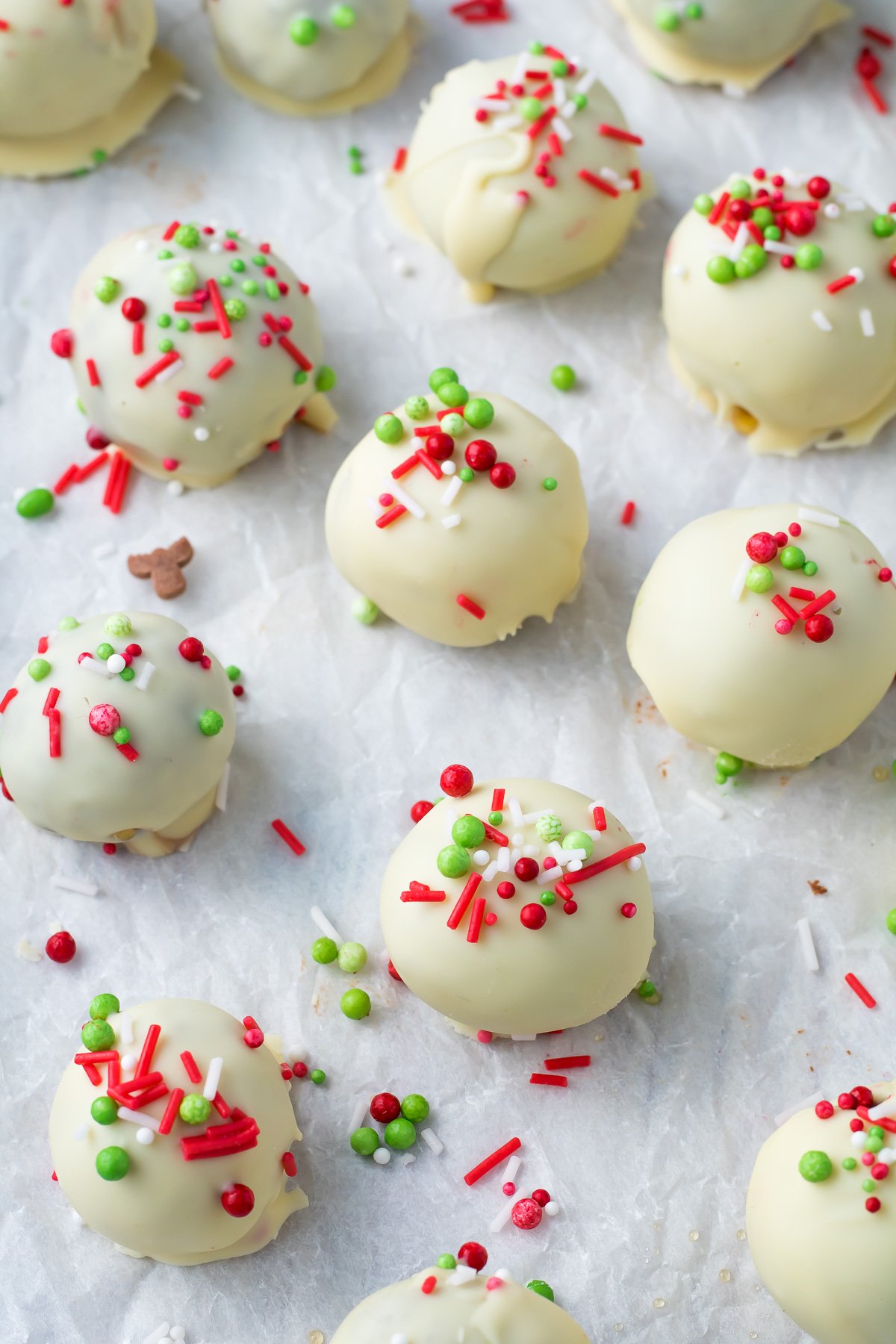 White chocolate Christmas truffles on parchment paper with sprinkles.