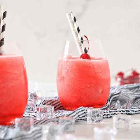 Two glasses of pink drinks with ice and straws on a table.