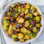 Overhead shot of air fryer brussels sprouts with bacon in a white bowl next to parmesan cheese.