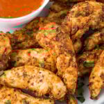 Air fryer chicken tenders with no breading on a plate with a small white bowl of buffalo sauce.