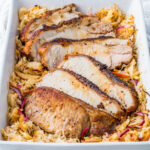 Pork and sauerkraut in a white casserole dish.