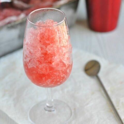 A glass of pink iced tea with a spoon next to it.