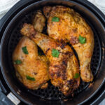 Chicken legs reheating in an air fryer basket.