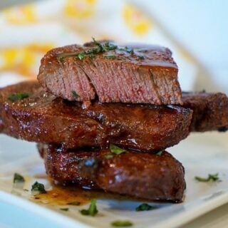 A stack of steaks on a plate in front of an air fryer.