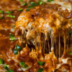 Spoon lifting heesy keto chicken enchilada casserole from dish.
