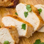 Sliced chicken breast on a wooden chopping board with parsley as a garnish.