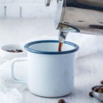 French press pouring espresso into a coffee cup.