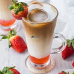 Strawberry latte on a table with strawberries, a white cloth, and another latte behind.