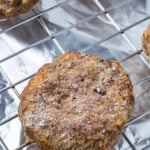 A frozen burger on a wire rack over aluminum foil on a baking sheet.
