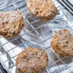 Frozen burgers on a wire rack over aluminum foil on a baking sheet.