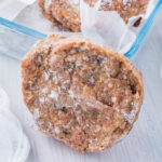 A frozen burger standing against a glass container of frozen hamburgers on a table with a cloth.