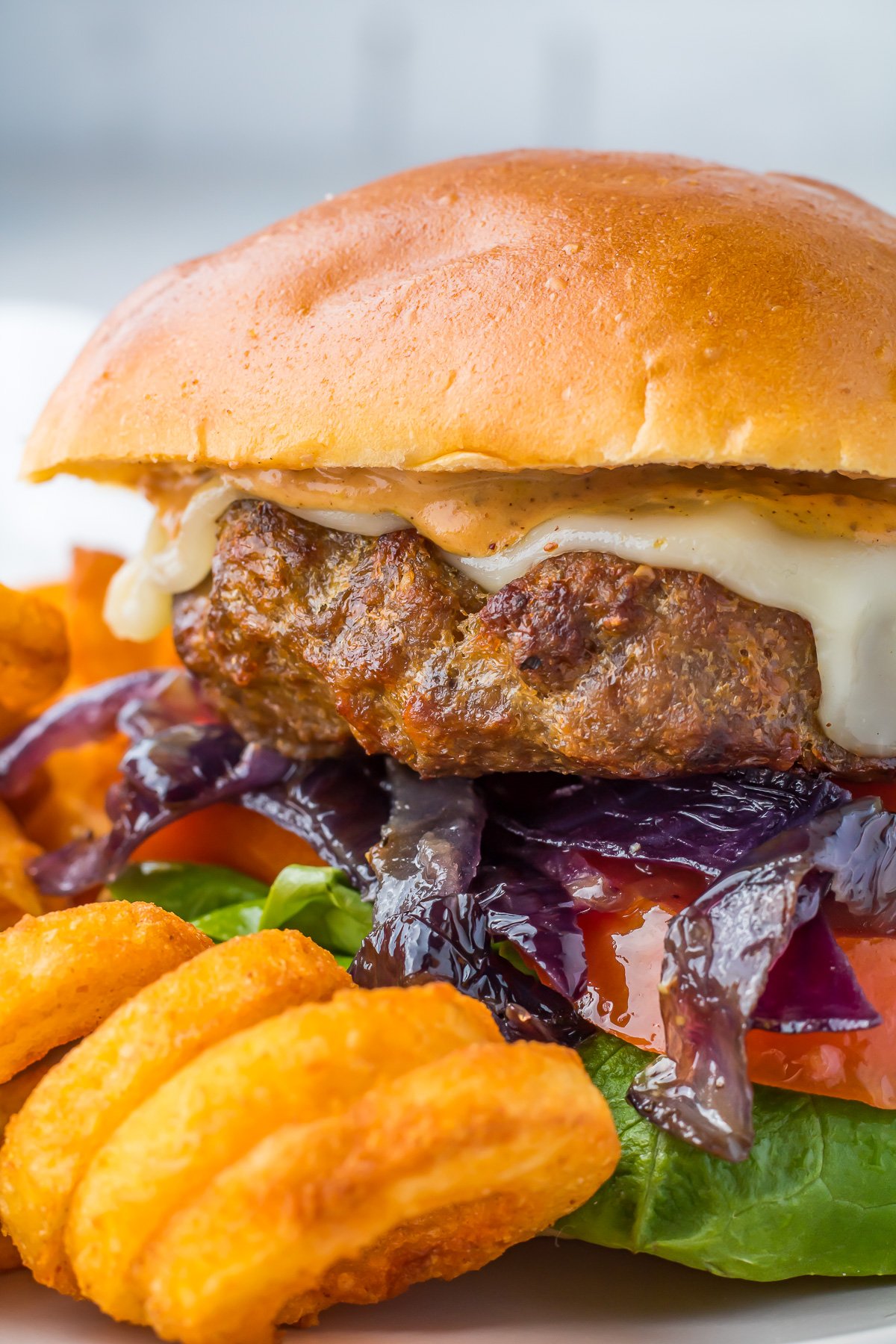 Hamburger on a grey plate with caramelized onions and curly fries.